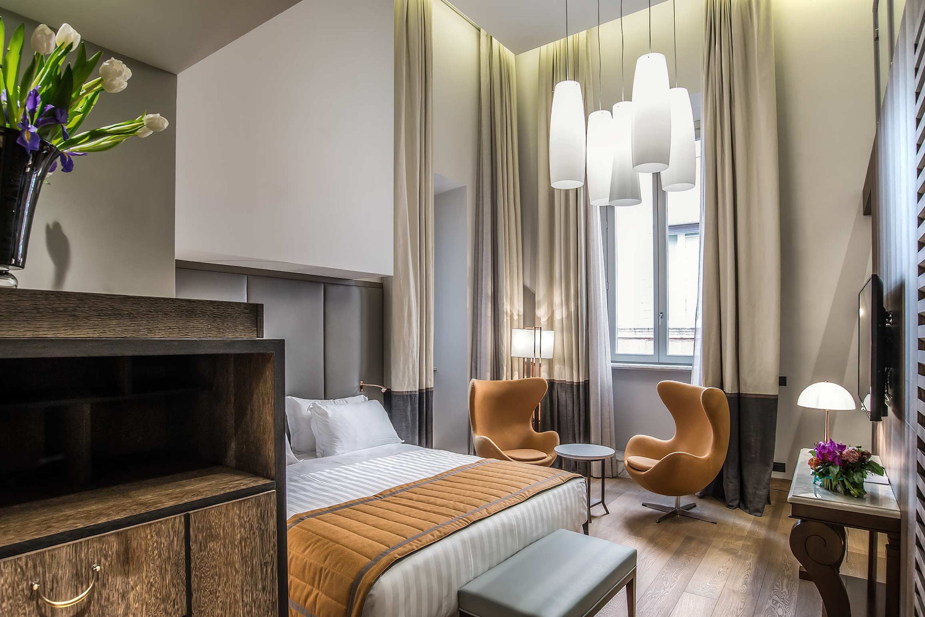 Une chambre d’hôtel avec un lit, un bureau, une chaise, une télévision et une fenêtre avec des rideaux.