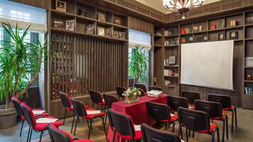 Una sala conferenze con un tavolo rosso, sedie nere, uno schermo per proiettore e scaffali.