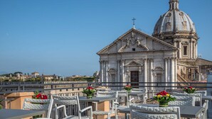 A terrace with white wicker furniture and flower arrangements, overlooking a historic building with a dome and classical architecture. - Martis Palace Hotel (Rome)