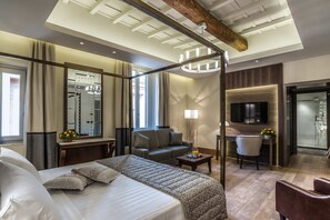 A hotel room with a large bed, a sofa, a desk with a chair, a TV, and a bathroom visible through a glass door. - Martis Palace Hotel (Rome)