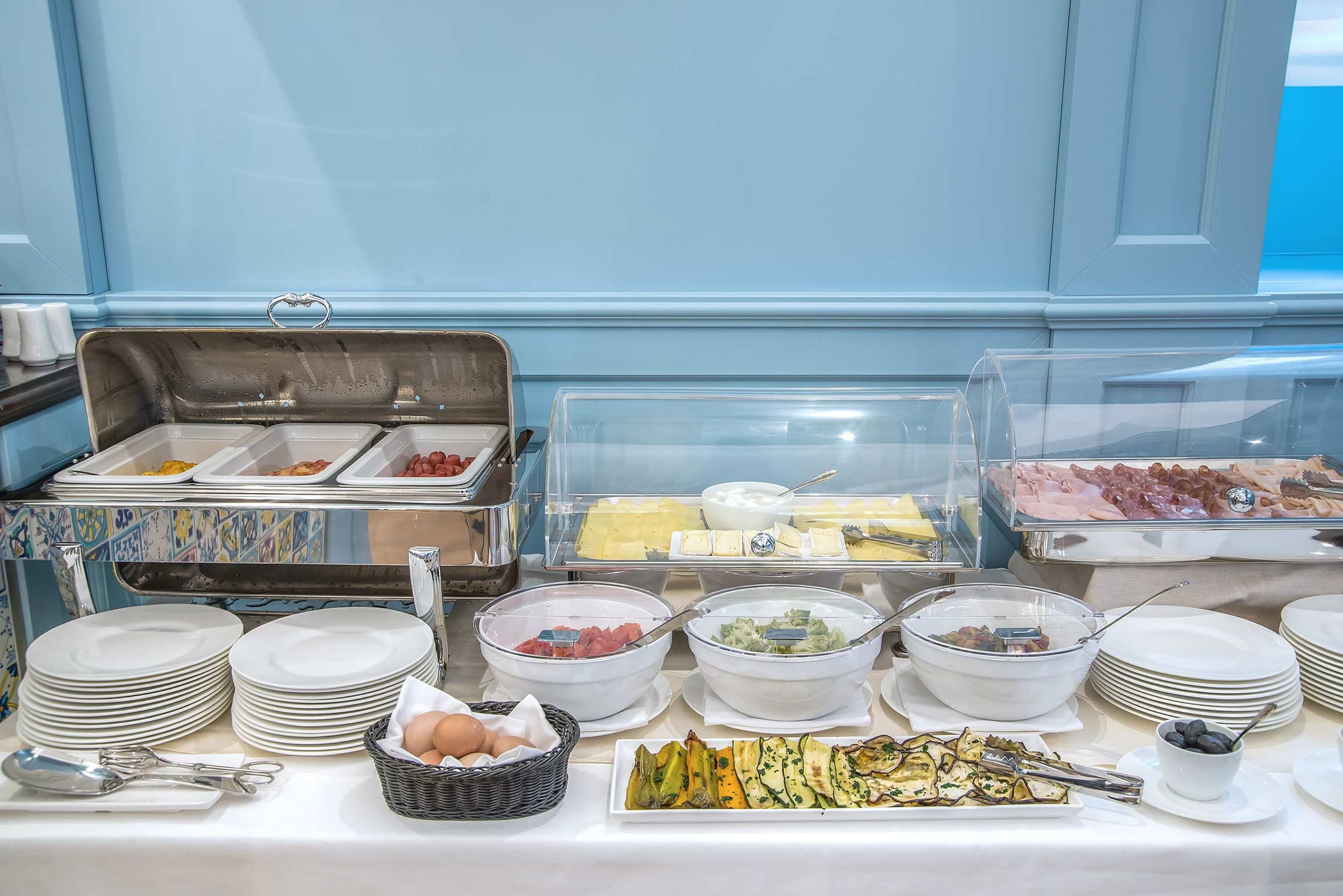 A buffet with various food items, including fruits, cheeses, and meats, arranged on a table with plates and bowls.