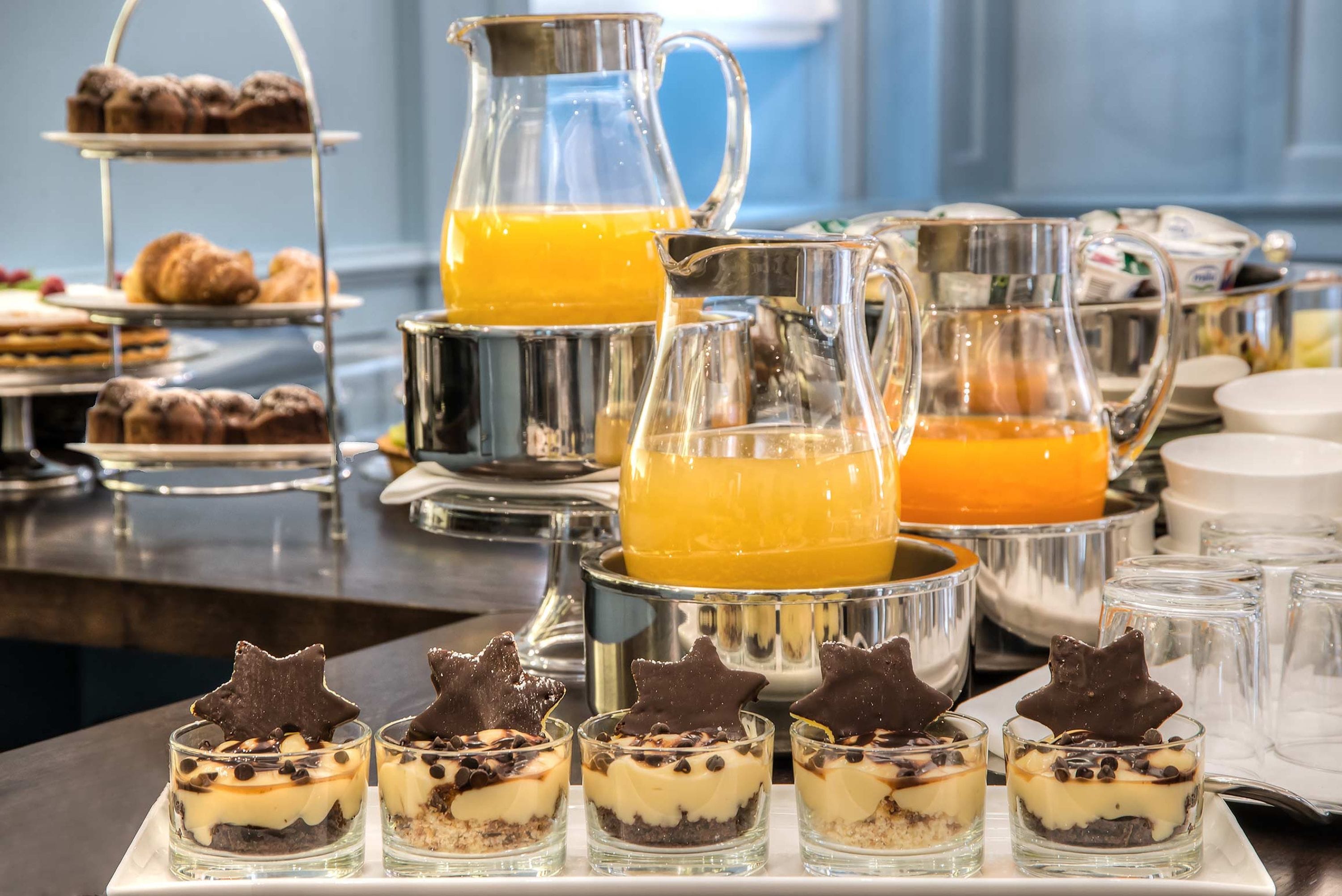 A buffet with desserts, a pitcher of orange juice, and a tiered stand with pastries.