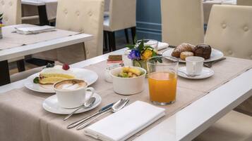 A breakfast setting with a plate of pastries, a cup of coffee, a bowl of fruit, and a glass of orange juice on a table.