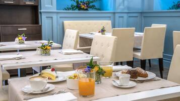 Un comedor con mesas dispuestas para el desayuno, incluyendo café, jugo, pasteles y un bol de fruta.