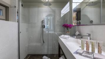 Ein modernes Badezimmer mit einer Duschkabine aus Glas, weißen Fliesenwänden, einem Waschbecken mit Spiegel und Pflegeprodukten.
