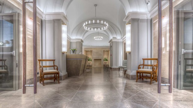 A spacious lobby with a high ceiling, a central reception desk, and two wooden chairs. - Martis Palace Hotel (Rome)