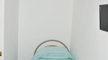 A small, narrow room with a single bed, a white wall, and a tiled floor.