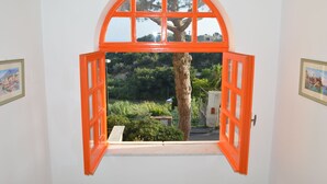 Habitación con ventana grande de diseño arqueado y marcos anaranjados, que ofrece vistas a un árbol y vegetación al exterior.