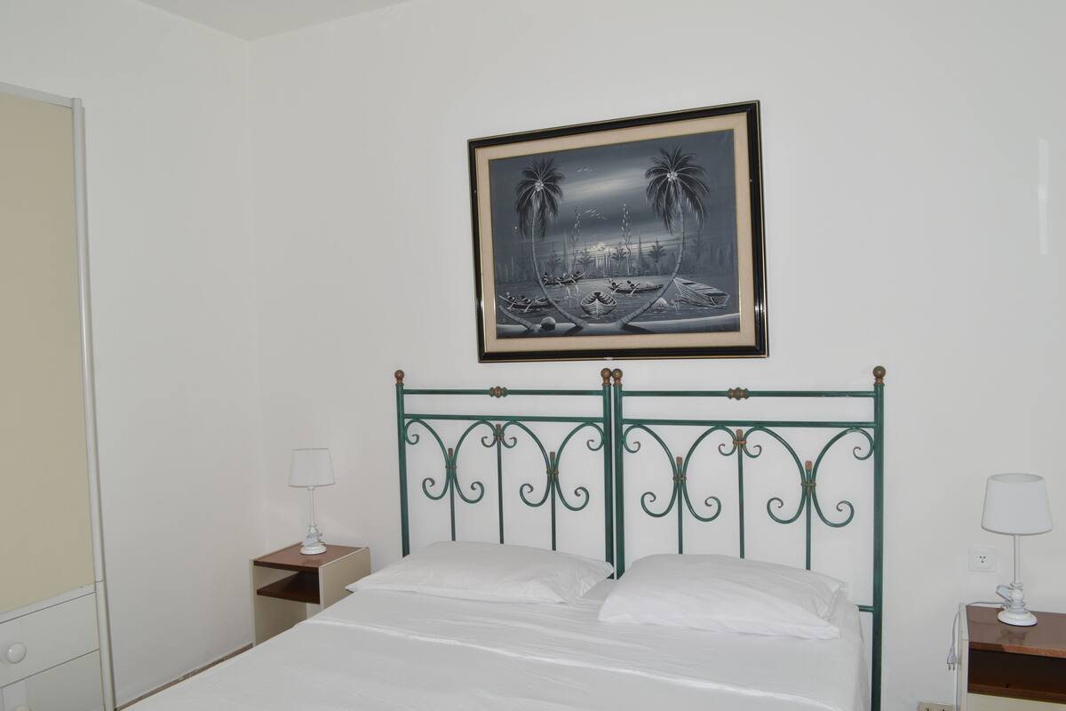 Un dormitorio con una cama, dos mesitas de noche, un cuadro enmarcado en la pared y un armario.
