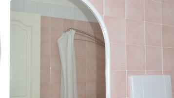 Un baño con puerta blanca, espejo, toallero y porta papel higiénico.