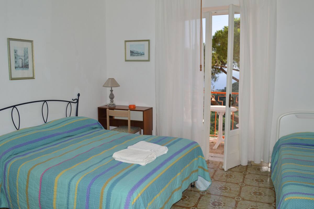 Un dormitorio con dos camas, una mesita de noche, una lámpara y vistas al exterior.