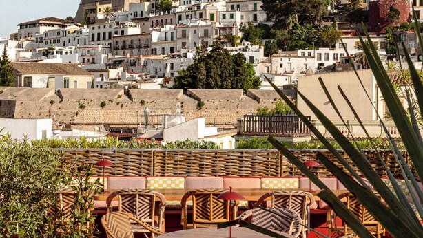 Eine Terrasse mit Korbmöbeln und Blick auf eine historische Stadt mit Gebäuden und einem markanten Turm.