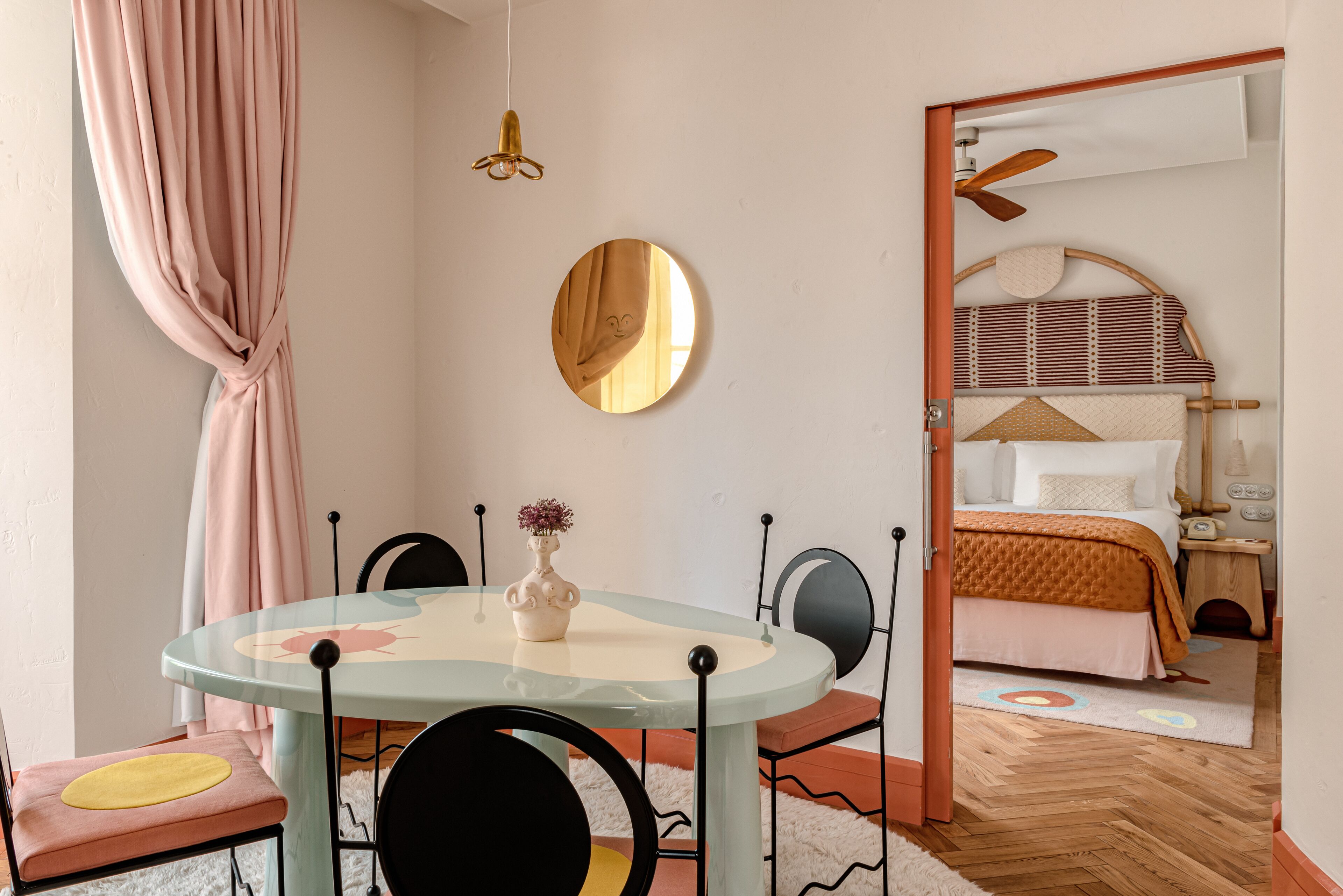 Una habitación acogedora con una mesa redonda, sillas, una cama con cabecera, un espejo y una lámpara colgante.