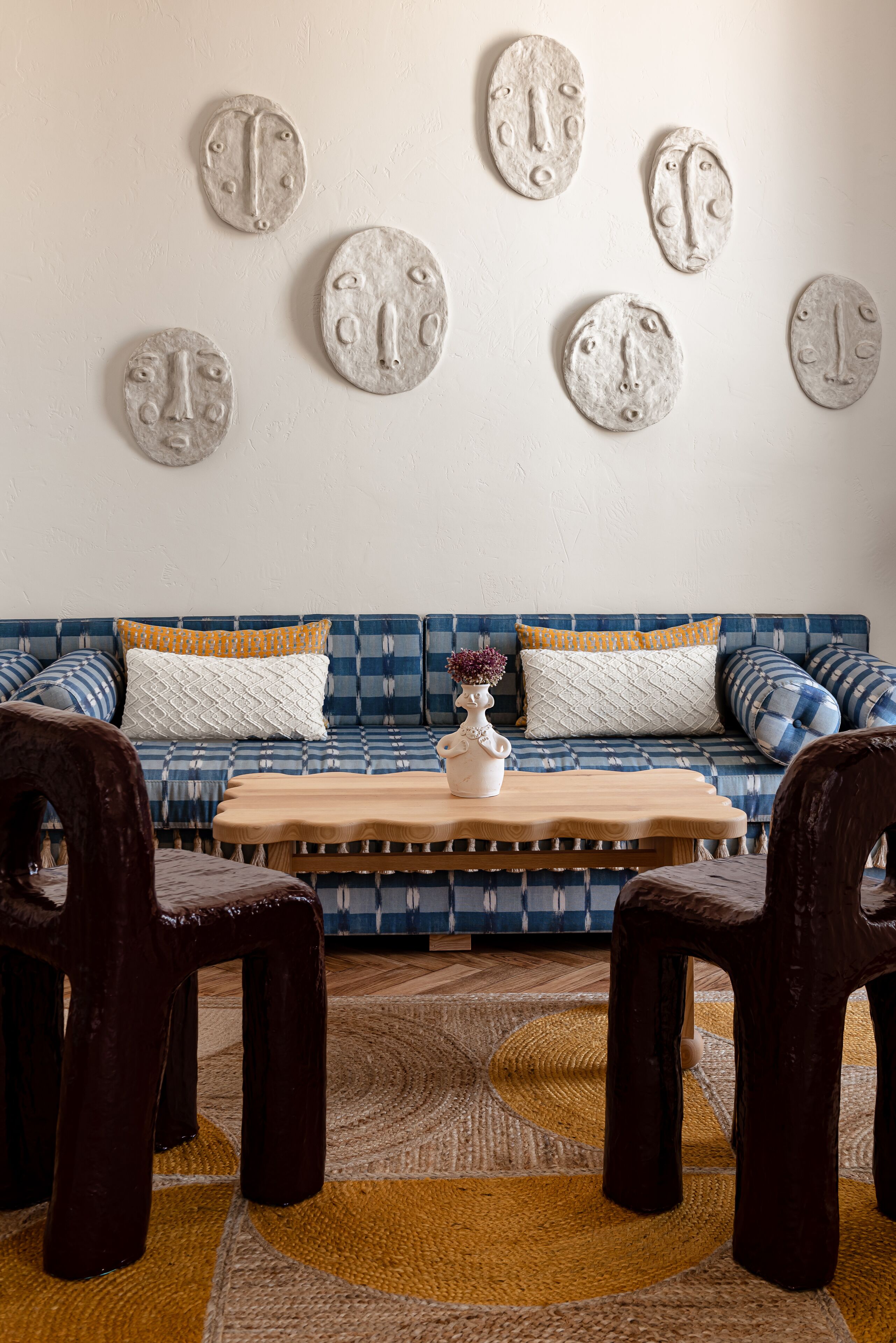 Un salon avec un canapé bleu à motifs, une table basse en bois et des fauteuils foncés.