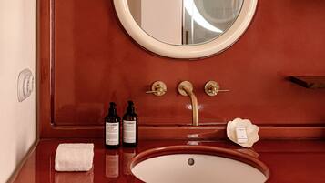 A bathroom with a wooden vanity, a round mirror with a tassel, a sink, and two bottles of lotion.