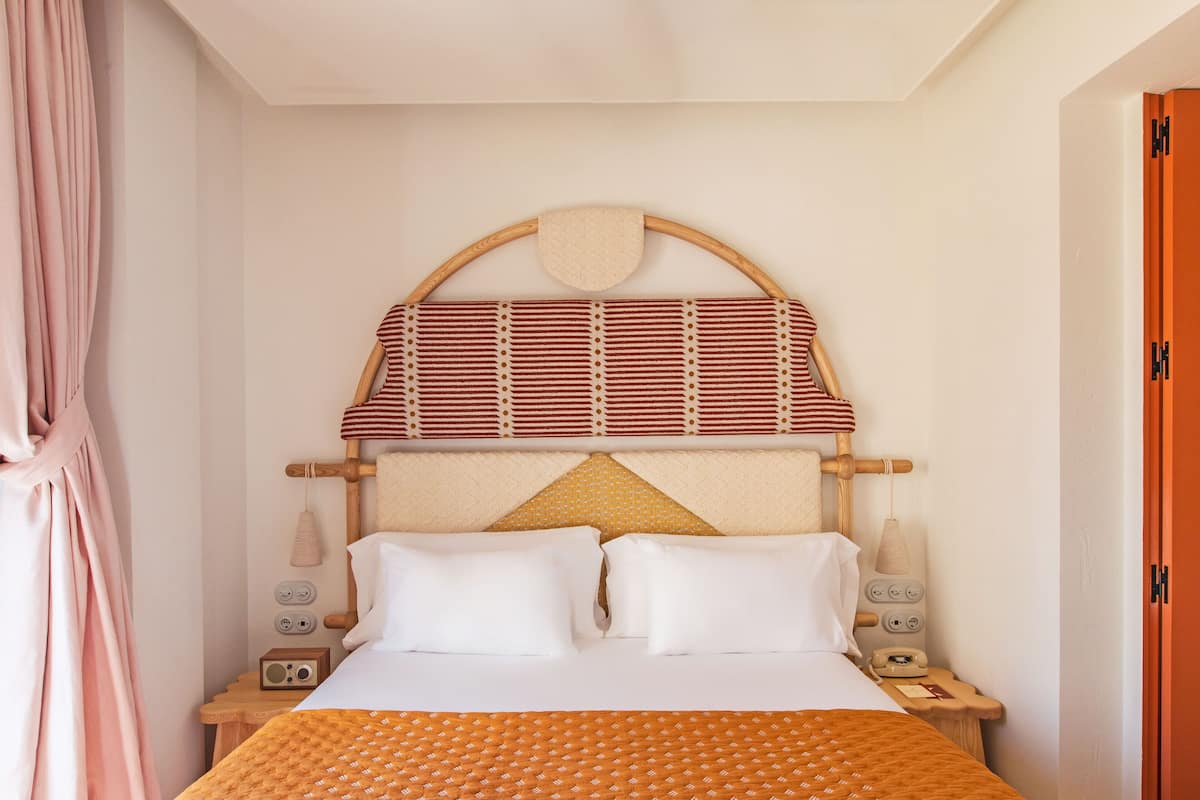 Habitació d'hotel ordenada amb un llit, dues taules de nit, una làmpada i un telèfon.