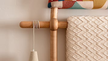 Una silla de madera con asiento y respaldo de mimbre, un cojín colorido y una lámpara fijada a la pared.