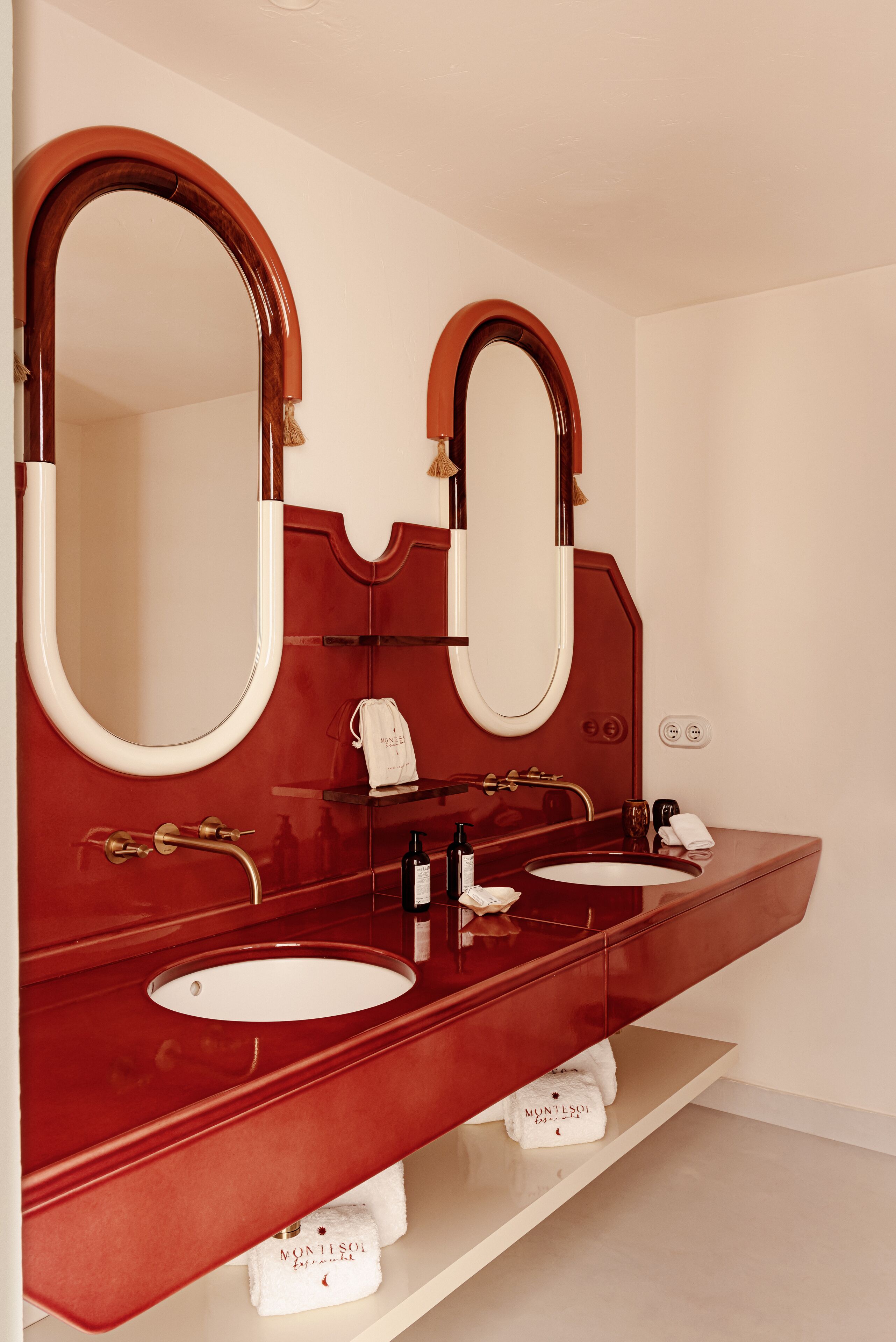 Un baño con dos lavamanos, un espejo grande y un tocador rojo.