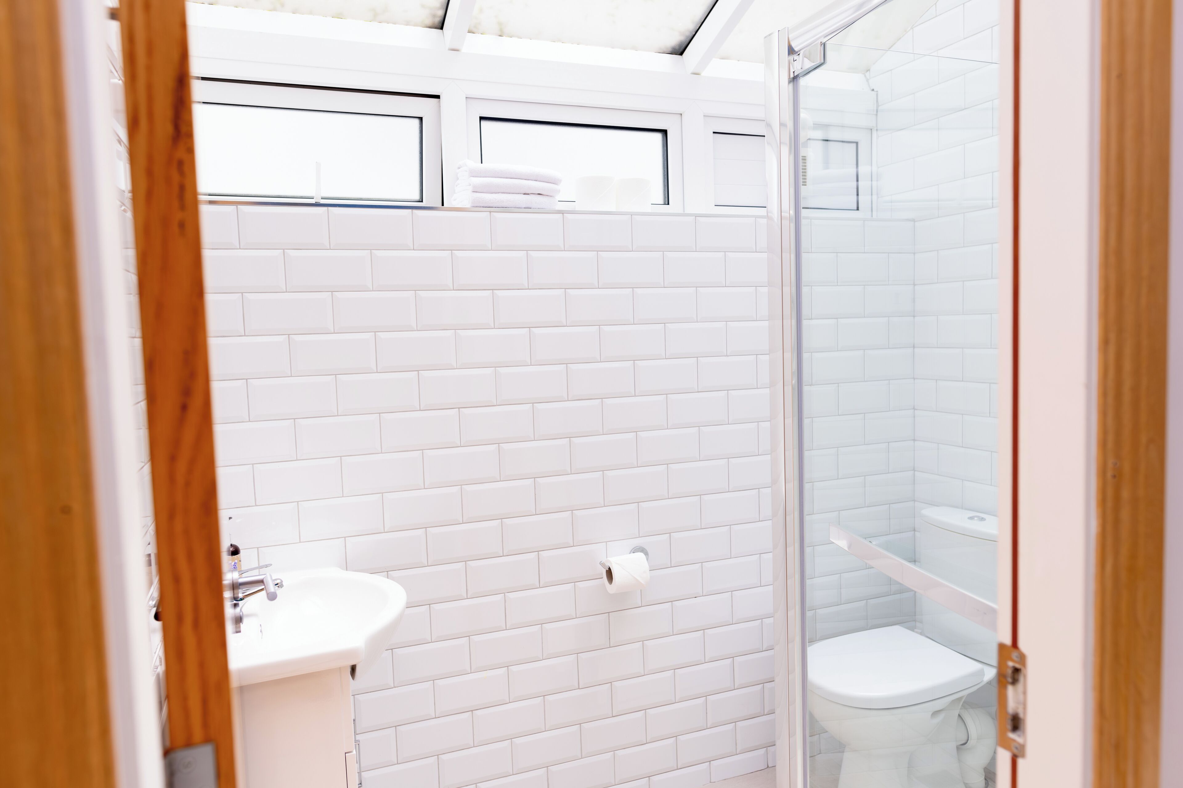 A bathroom with white tiled walls, a sink, a toilet, and a glass shower enclosure.
