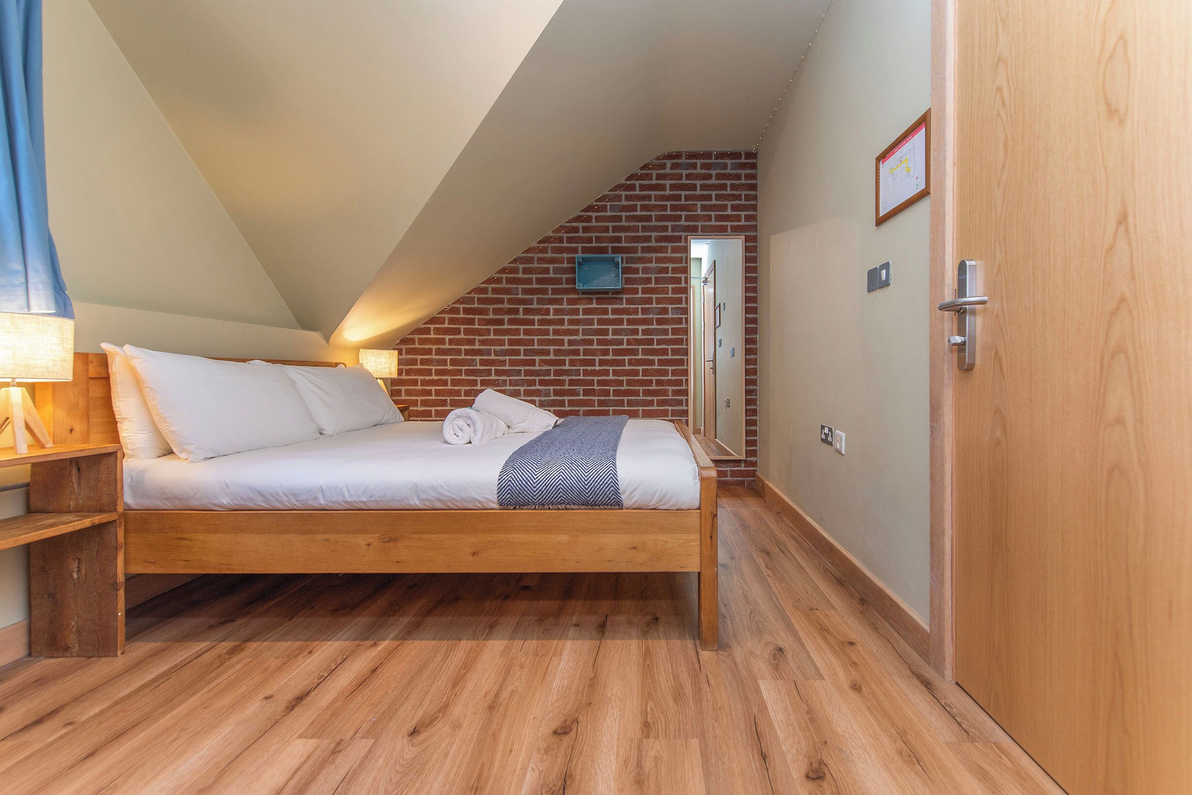 A bedroom with a wooden bed, a brick wall, and a door.
