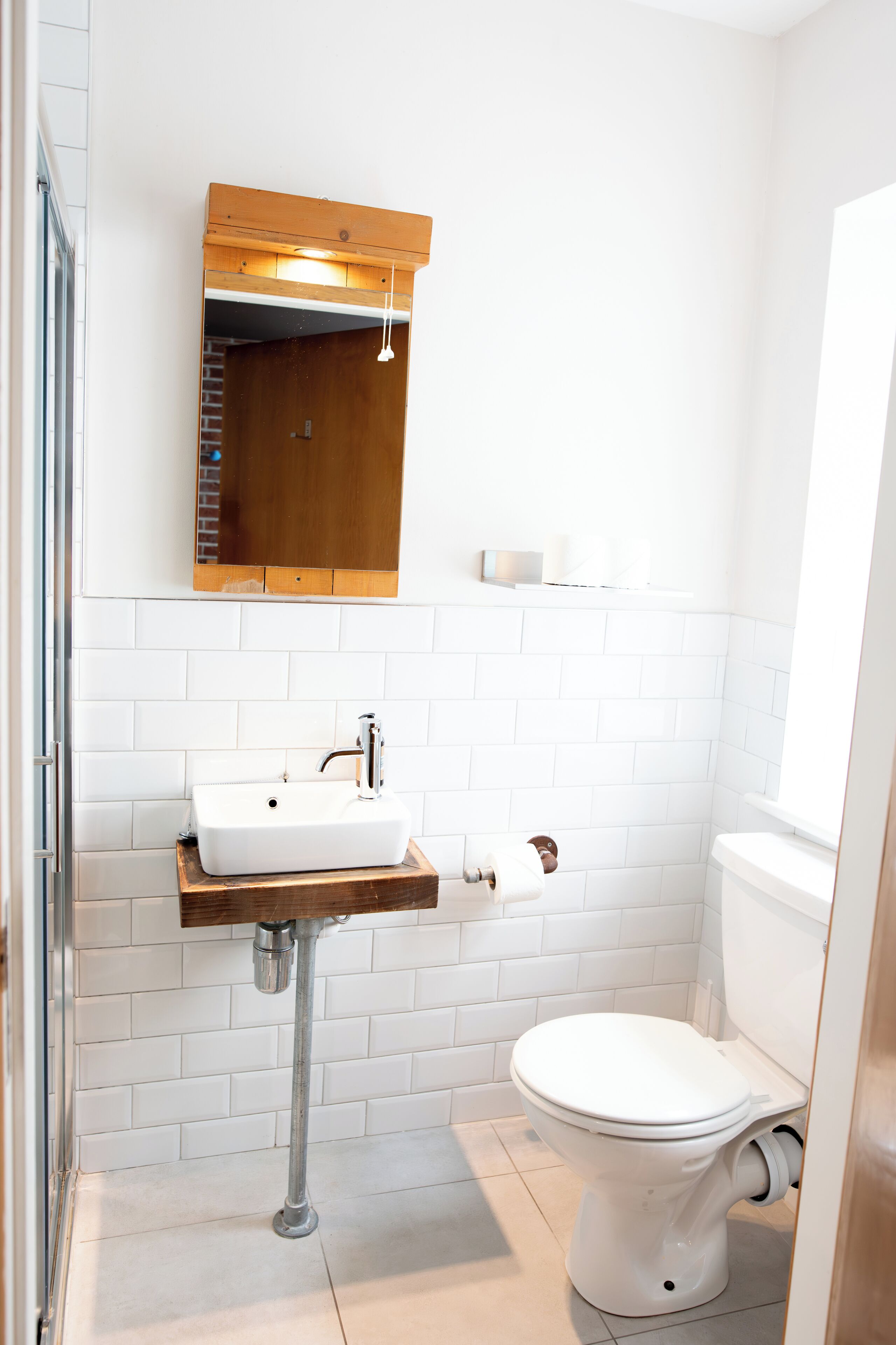 Une salle de bain avec un lavabo blanc, un meuble-lavabo en bois, un miroir, des toilettes et un espace douche.