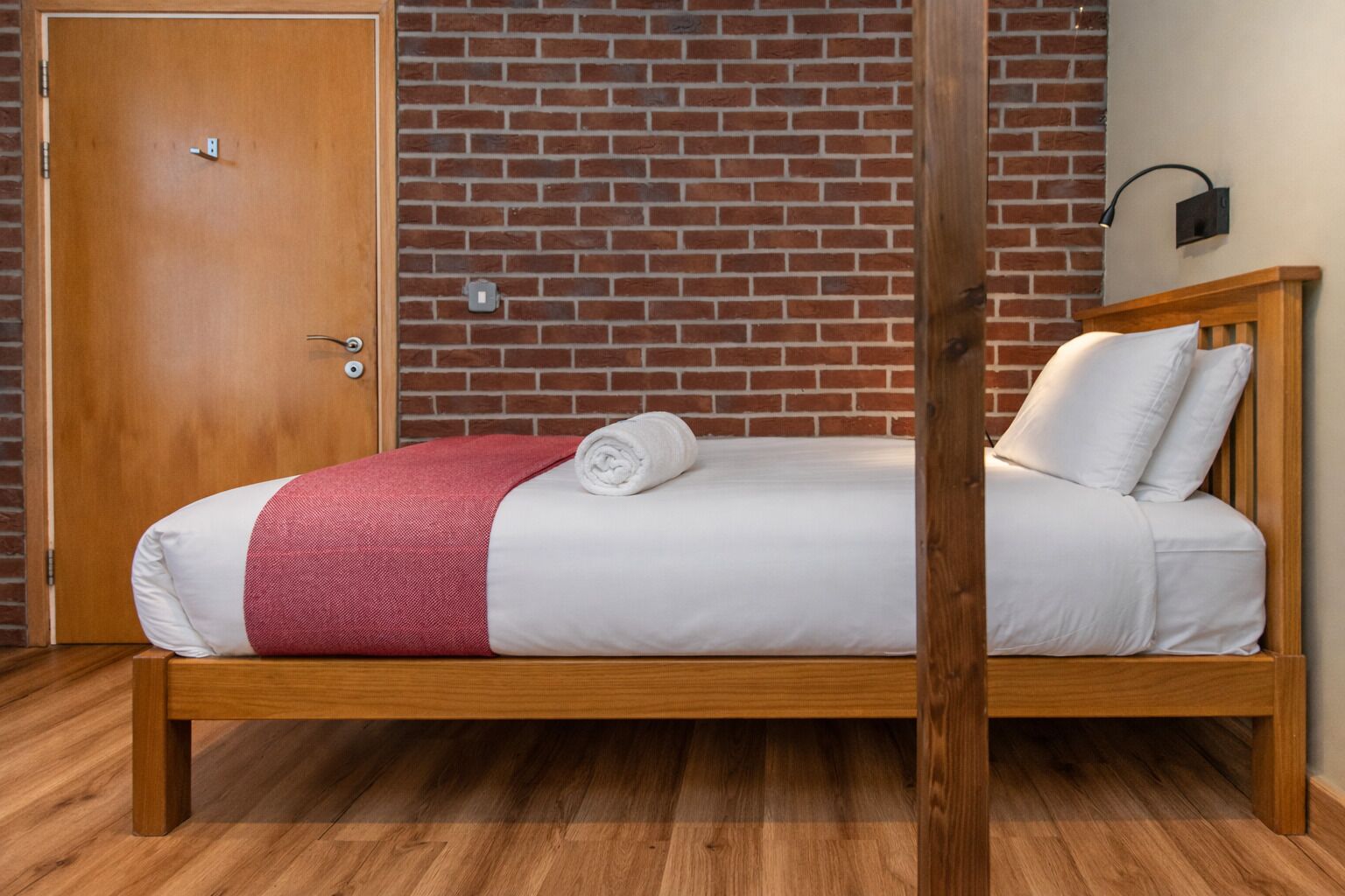 Un lit simple avec un cadre en bois, une couverture rouge et un oreiller blanc.