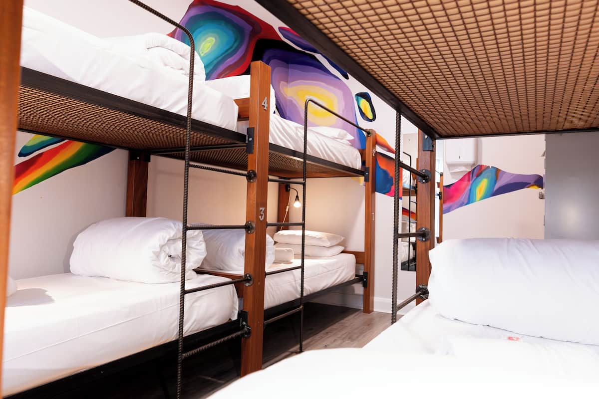 Habitación con literas de madera, ropa de cama blanca y un mural abstracto y colorido en la pared.