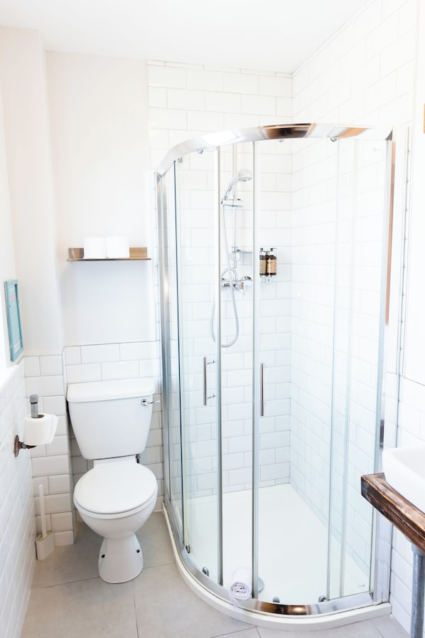 A modern bathroom with a glass-enclosed shower, a white toilet, and a wooden vanity. - The Nest Boutique Hostel (Galway)