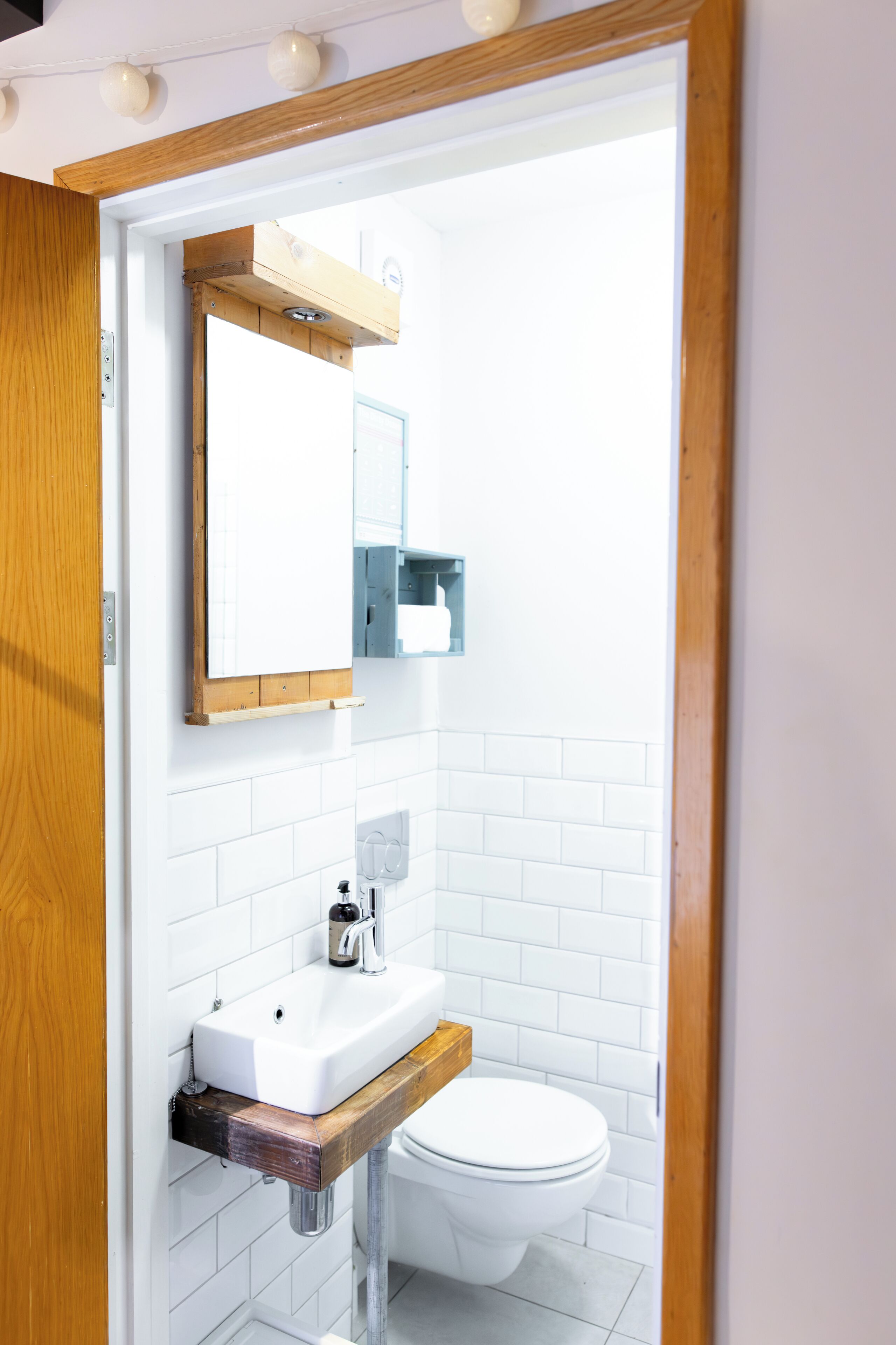 A bathroom with a wooden-framed mirror, white tiled walls, a white sink, and a toilet.