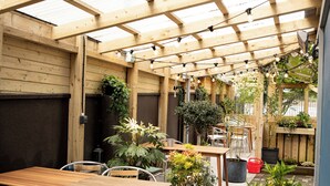 Une terrasse extérieure avec des tables et des chaises en bois, des plantes en pot et des guirlandes lumineuses.