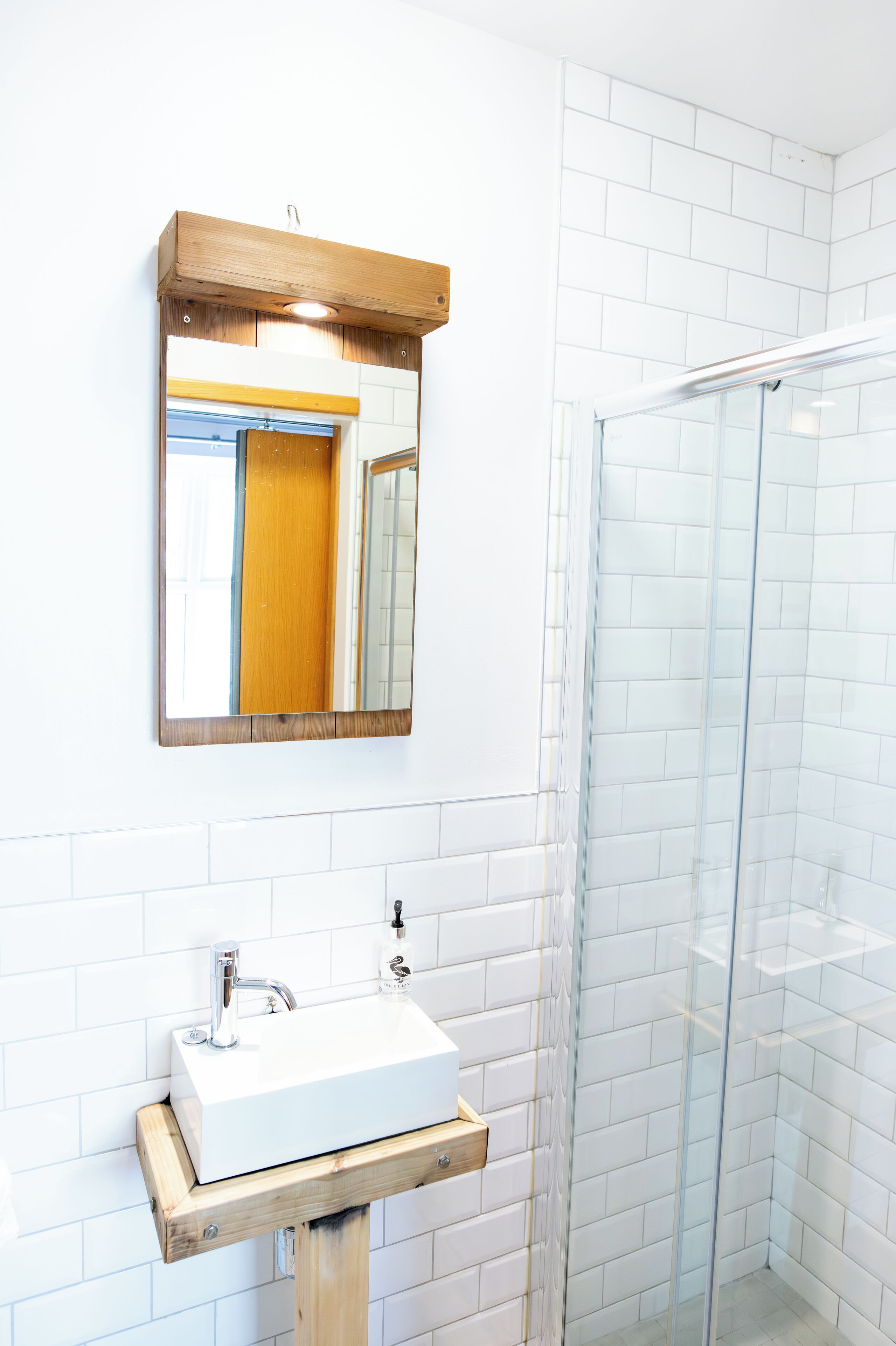 A bathroom with a white sink, a wooden-framed mirror, and a glass shower enclosure.