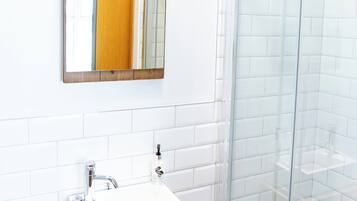 A bathroom with a white sink, a wooden-framed mirror, and a glass shower enclosure.