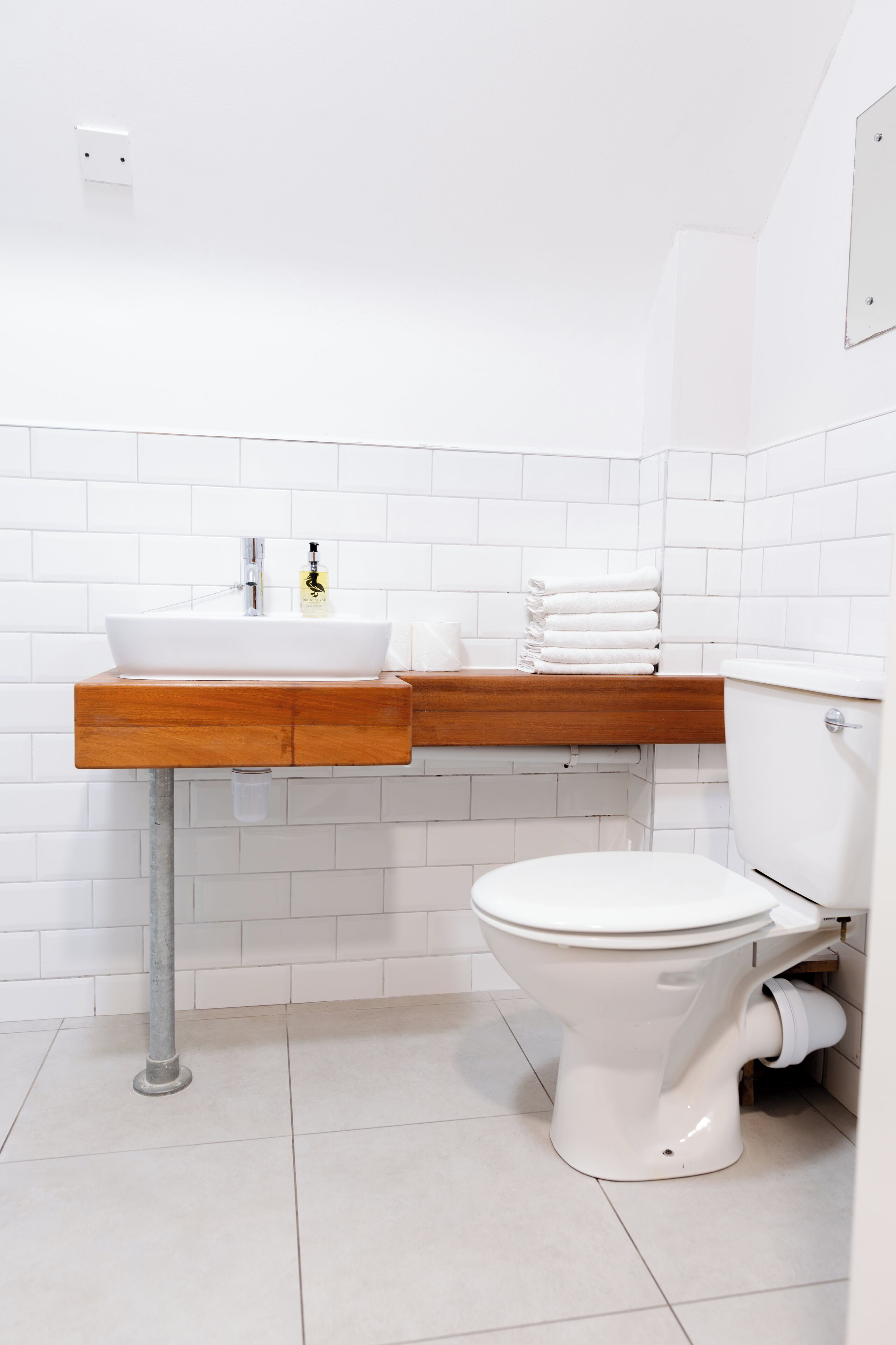 A bathroom with a white sink, wooden vanity, white toilet, and white tiled walls.