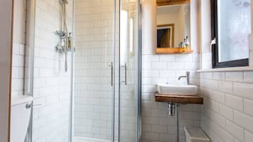 Une salle de bain moderne avec une douche à parois de verre, des murs recouverts de carreaux blancs, un lavabo en bois et un miroir au-dessus du lavabo.