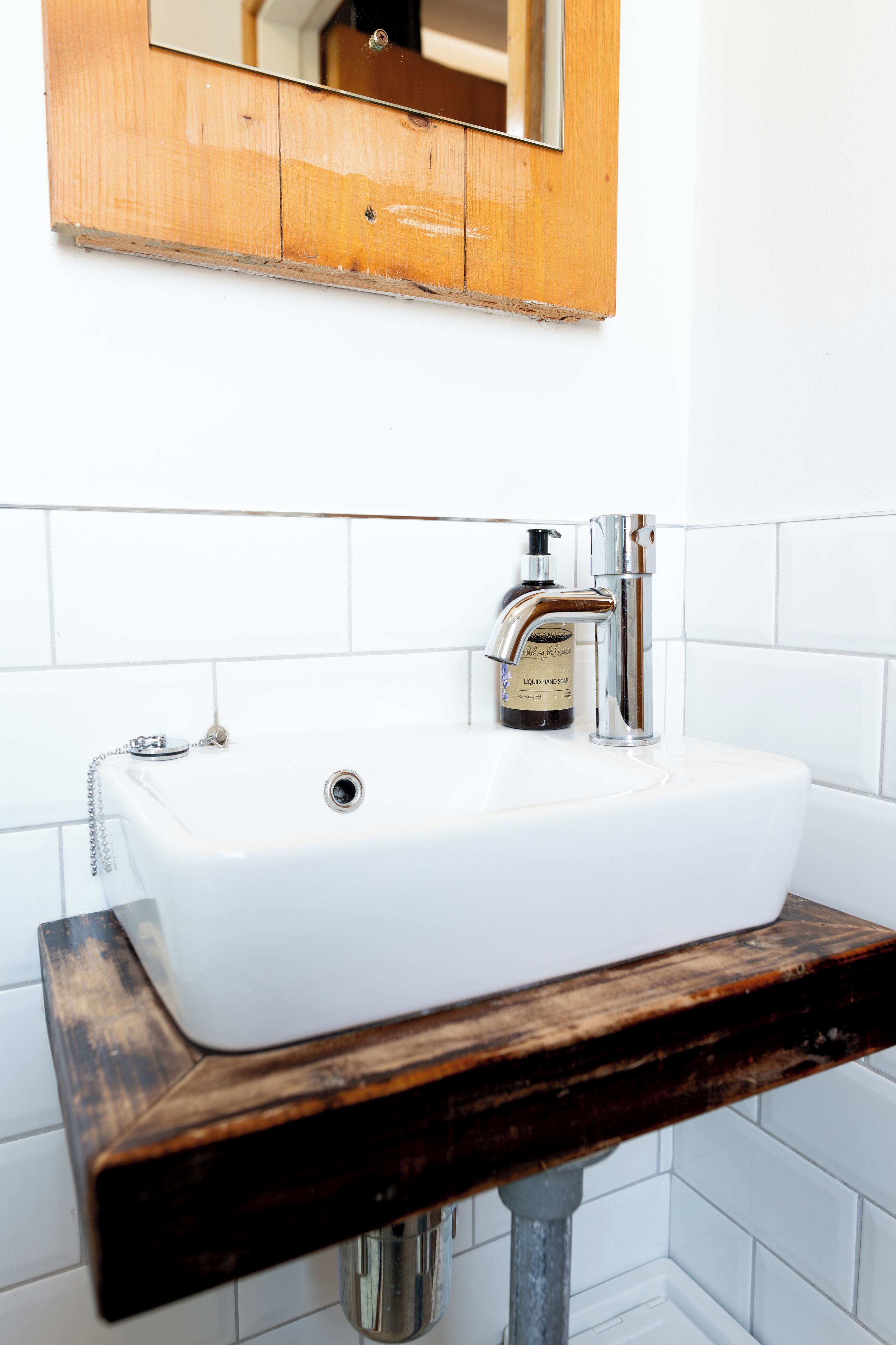 Un baño con lavamanos blanco, grifo cromado y repisa de madera.