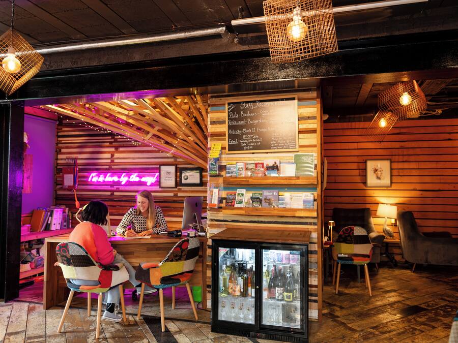 A cozy restaurant with wooden walls, a neon sign, and a menu board. There are chairs and a refrigerator with drinks.