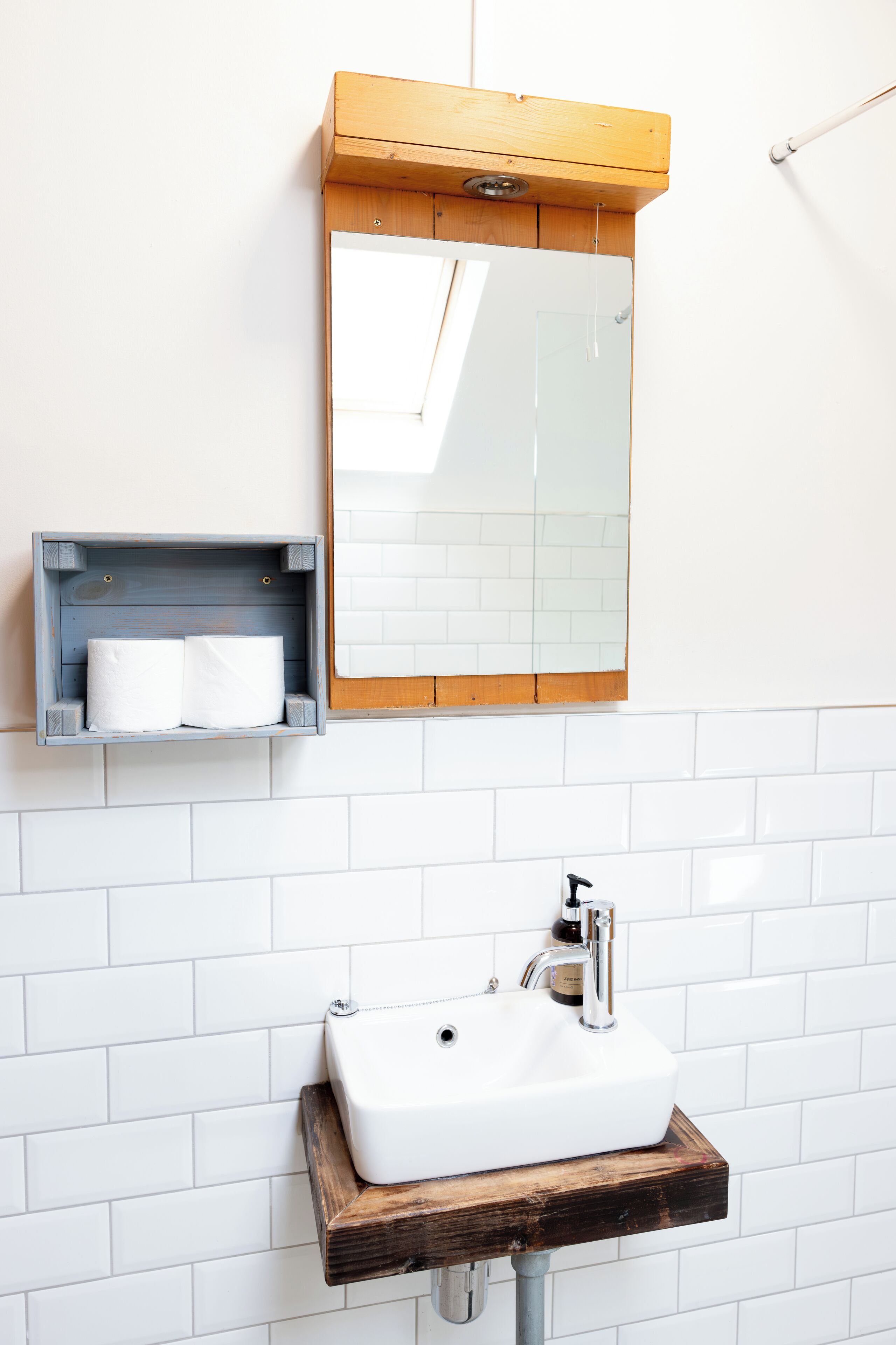 A bathroom with a white sink, wooden shelf, and a mirror.