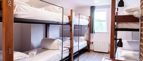 A bunk bed room with wooden frames, white bedding, and a window with curtains.