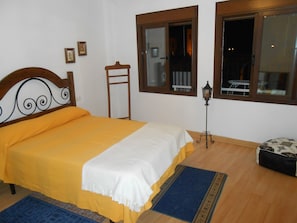 Un dormitorio con una cama, cabecera de madera, mesita de noche, lámpara, ventana y una pequeña mesa.