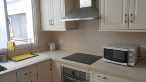 Een keuken met witte kastjes, een magnetron, een oven en een raam met zonwering.