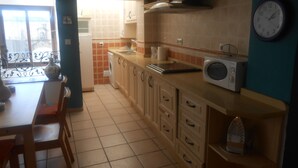 Een keuken met een eettafel, stoelen, een magnetron en een klok aan de muur.