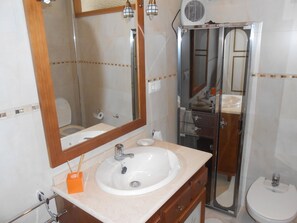 Un baño con lavamanos blanco, espejo, ducha e inodoro.