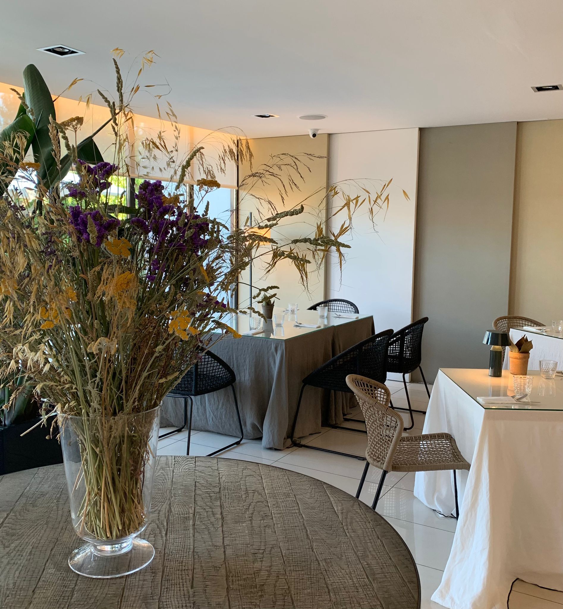 Een eetgedeelte met een ronde tafel, stoelen en een vaas met gedroogde bloemen.