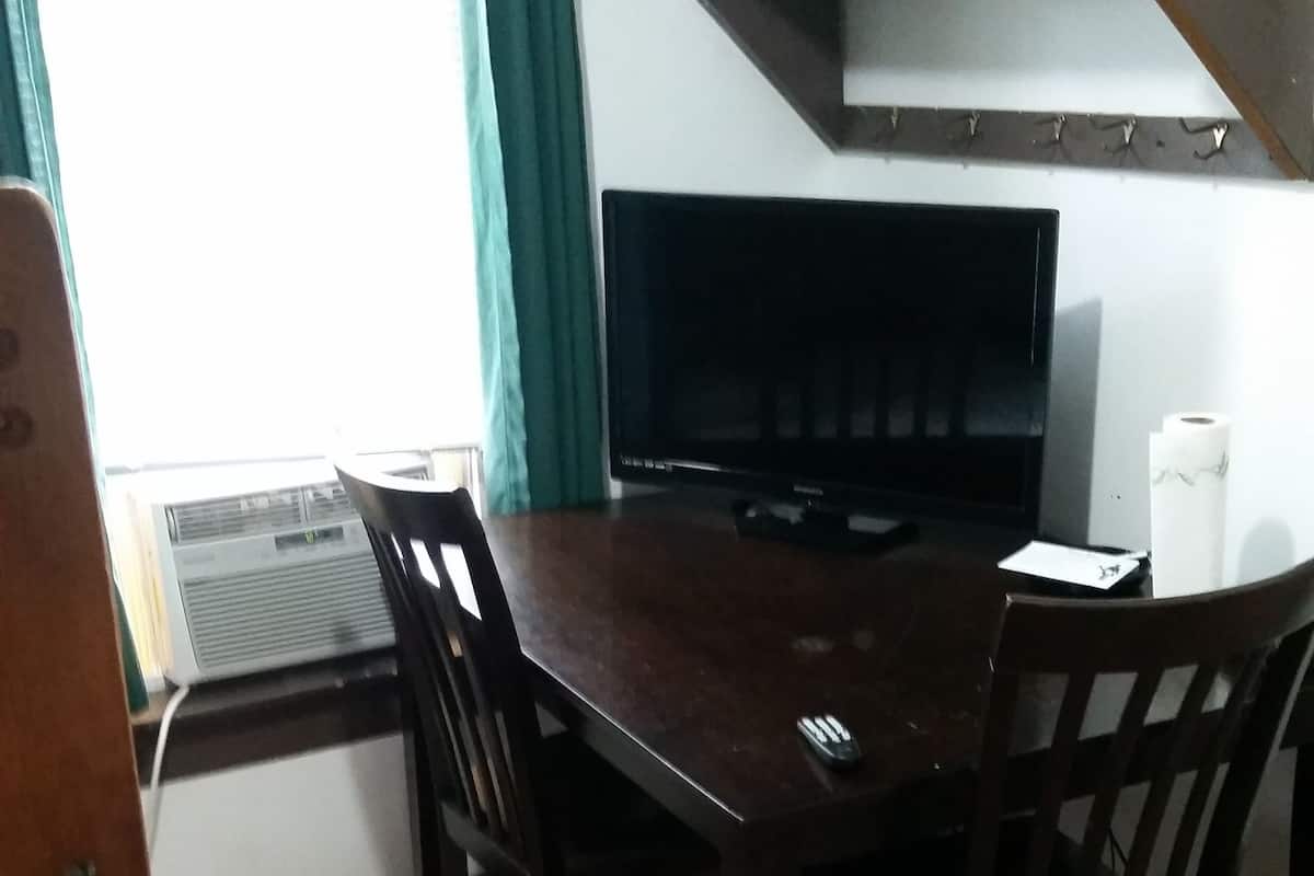 A dining area with a dark wooden table and chairs, a television on the wall, and a window with curtains.