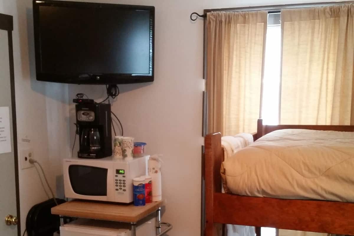 A compact room with bunk beds, a television, a microwave, a coffee maker, and a small trash bin.