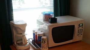 A kitchenette with a coffee maker, microwave, and storage containers. - The School House Inn (Altmar)