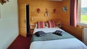 A wooden-paneled bedroom with a bed, two bedside tables, red lamps, and a window with curtains.