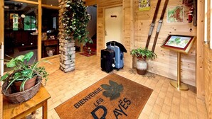 A wooden interior with a stone pillar, a doormat, a basket of plants, and a sign on the wall.
