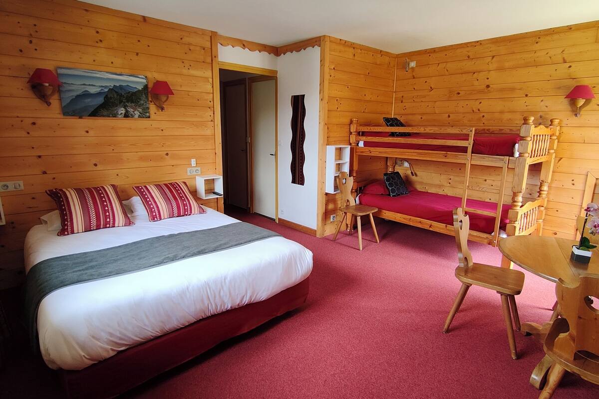 Ein holzgetäfelter Raum im Blockhausstil mit einem großen Bett, einem Schlafstockbett, einem kleinen Tisch und einem Stuhl.