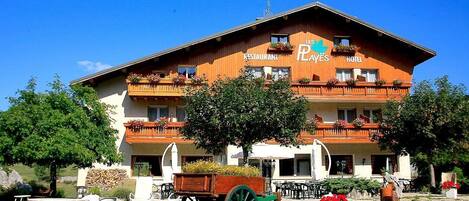 A two-story building with a restaurant and hotel sign, outdoor seating, and a wooden cart.